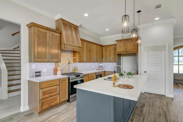 kitchen featuring sink, stainless steel gas range, light hardwood / wood-style flooring, premium range hood, and a center island with sink