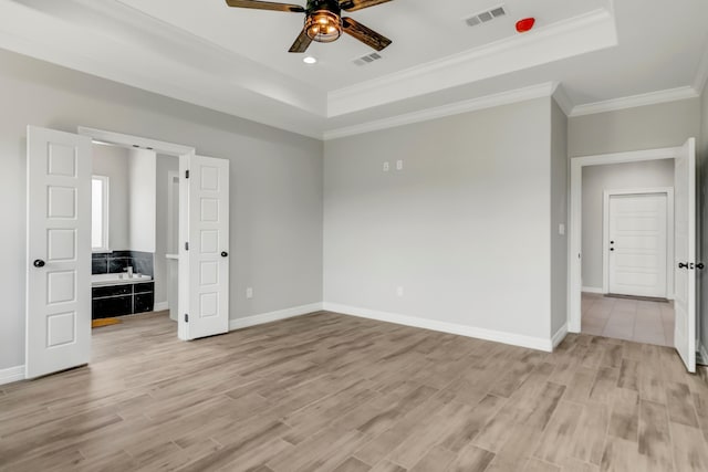 interior space with crown molding, ensuite bath, ceiling fan, light wood-type flooring, and a tray ceiling