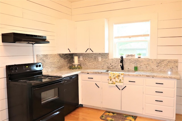 kitchen with ventilation hood, sink, black appliances, white cabinetry, and wood walls