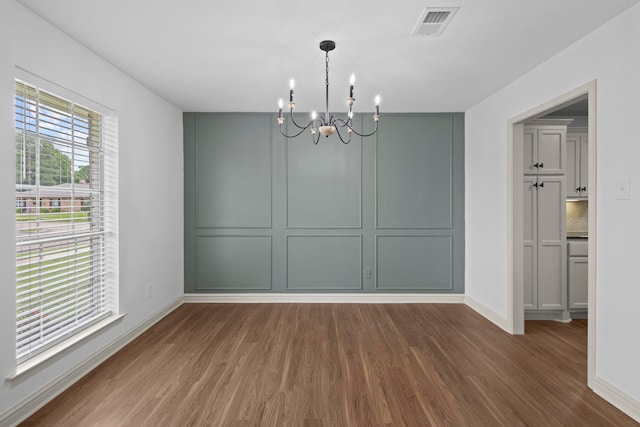 unfurnished dining area with wood finished floors, visible vents, baseboards, and a notable chandelier