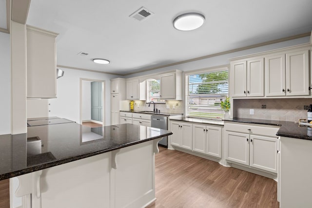 kitchen with a peninsula, a sink, visible vents, a kitchen bar, and light wood-style floors