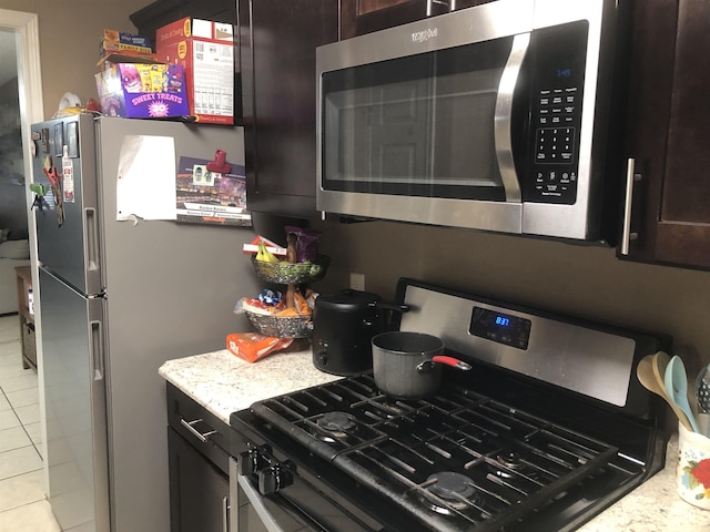 kitchen featuring light tile patterned floors, dark brown cabinetry, and appliances with stainless steel finishes