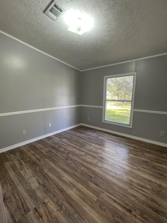 spare room featuring ornamental molding, dark wood-type flooring, and a textured ceiling