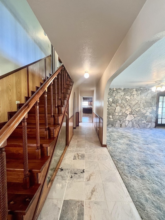 corridor featuring wood walls, light colored carpet, and a textured ceiling