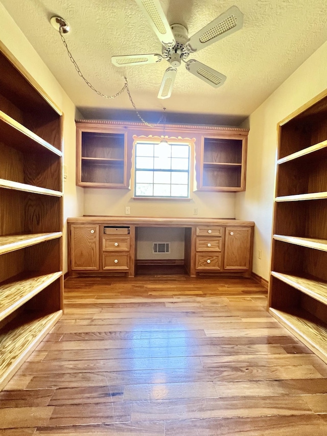 unfurnished office with ceiling fan, light wood-type flooring, built in desk, and a textured ceiling