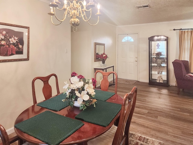 dining area featuring hardwood / wood-style flooring, a textured ceiling, crown molding, and an inviting chandelier