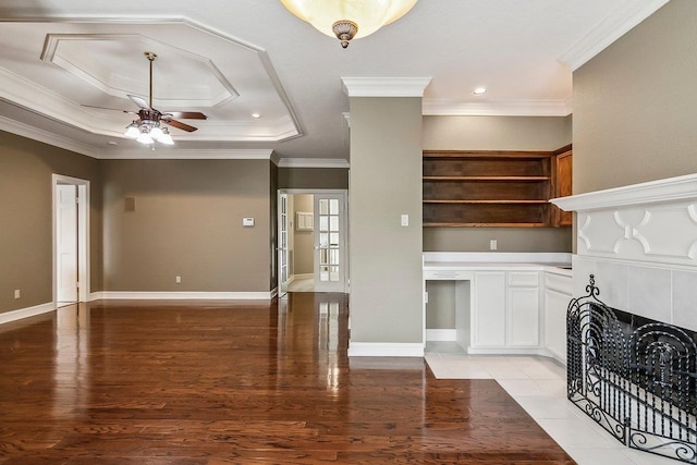 unfurnished living room with a tiled fireplace, crown molding, ceiling fan, and a tray ceiling