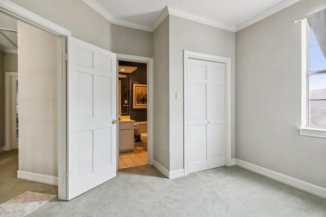 unfurnished bedroom with crown molding, light colored carpet, ensuite bathroom, and a closet