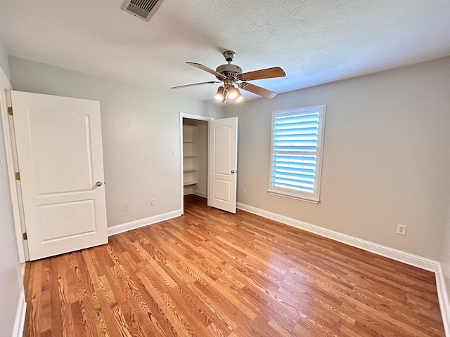 unfurnished bedroom with a walk in closet, ceiling fan, light hardwood / wood-style floors, and a textured ceiling