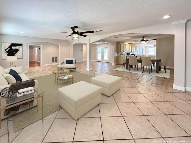 tiled living room featuring ceiling fan, french doors, and a textured ceiling