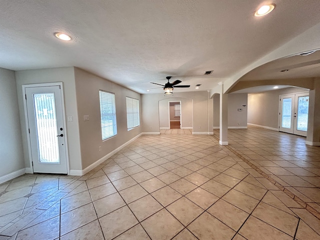 unfurnished living room with ceiling fan, light tile patterned flooring, a textured ceiling, and french doors