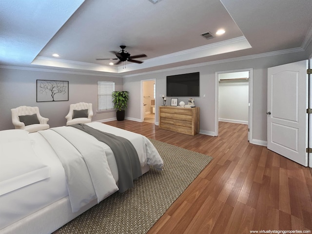 bedroom featuring a raised ceiling, ensuite bath, ornamental molding, and ceiling fan