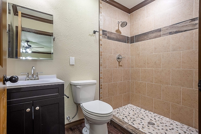 bathroom with tiled shower, vanity, toilet, and ceiling fan