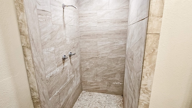 full bath featuring tiled shower and a textured wall