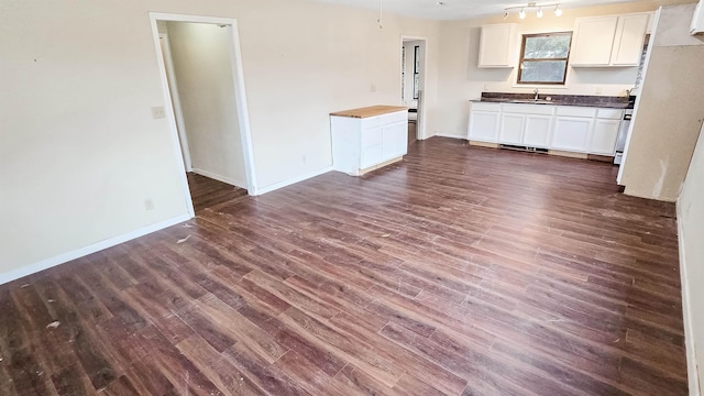 kitchen with dark wood-style flooring, white cabinetry, a sink, and baseboards