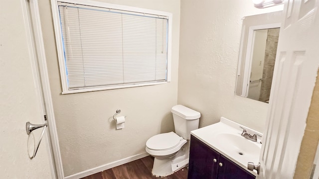 bathroom with a textured wall, toilet, wood finished floors, vanity, and baseboards