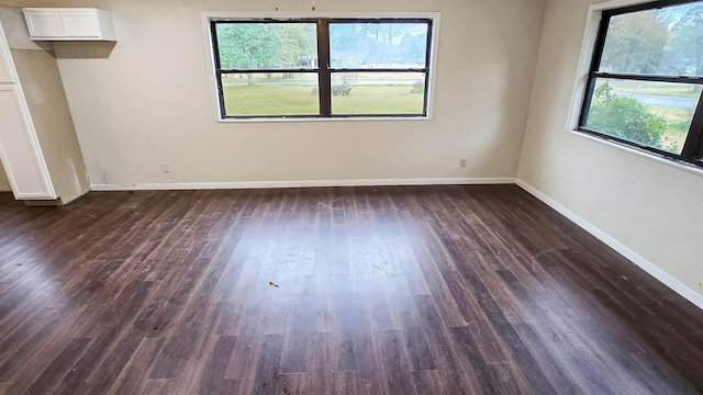 spare room featuring baseboards and dark wood-type flooring