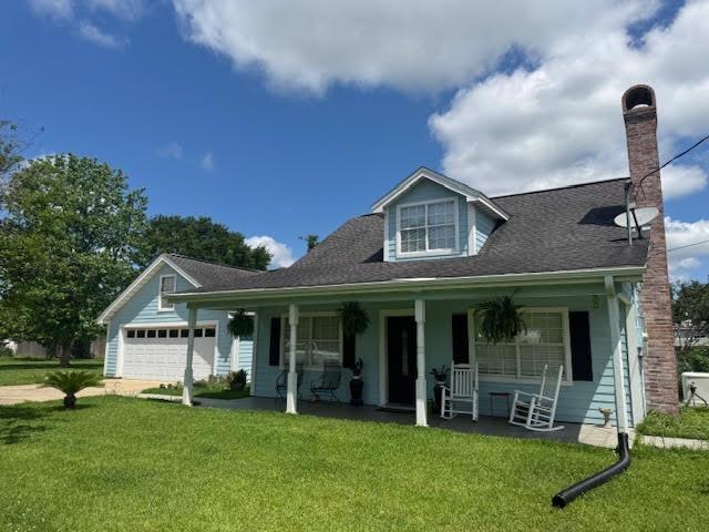 view of front facade featuring a chimney, a front yard, a porch, and a garage