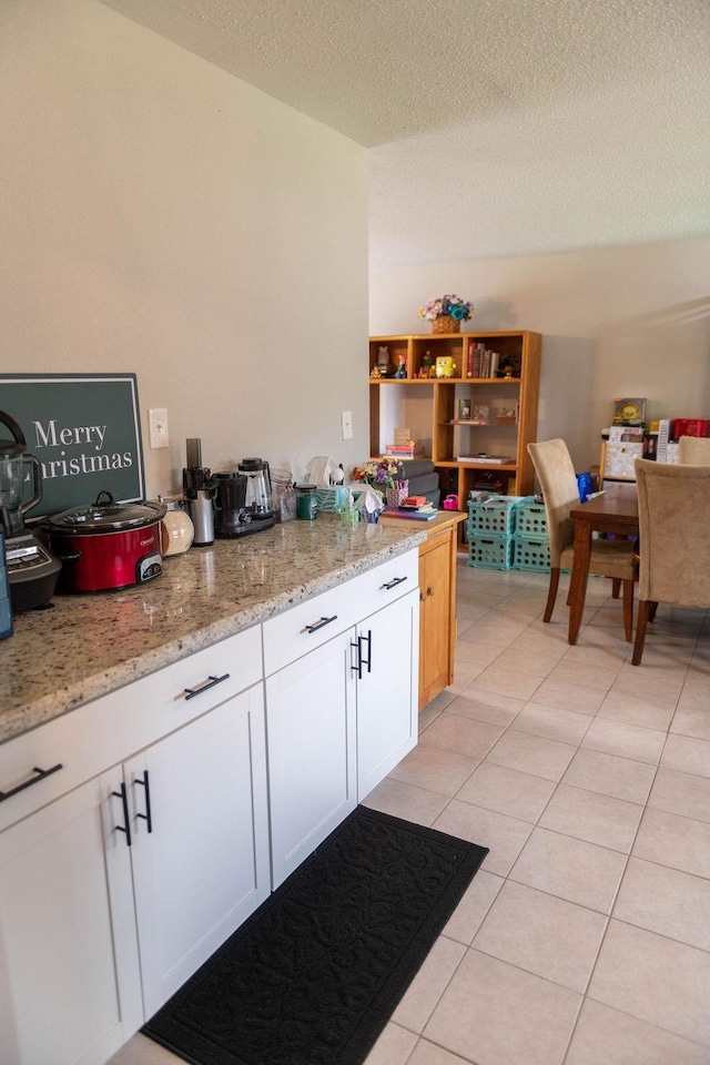 kitchen featuring white cabinets, light stone countertops, a textured ceiling, and light tile patterned floors