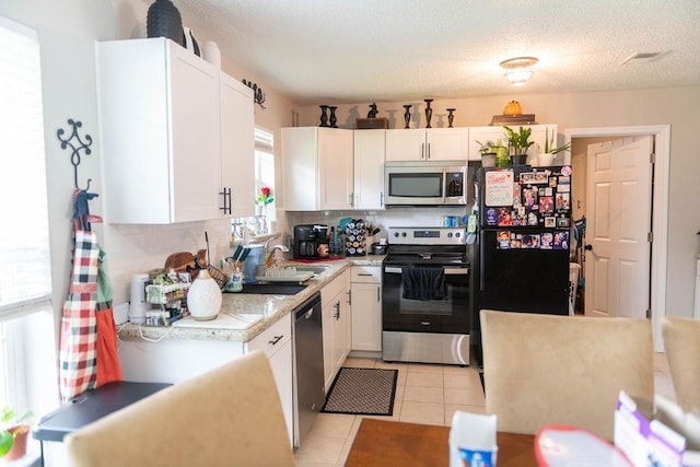 kitchen featuring backsplash, white cabinets, sink, light tile patterned flooring, and stainless steel appliances