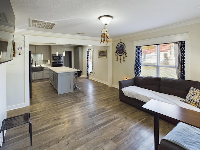 living room featuring ornamental molding, a textured ceiling, sink, a chandelier, and dark hardwood / wood-style floors