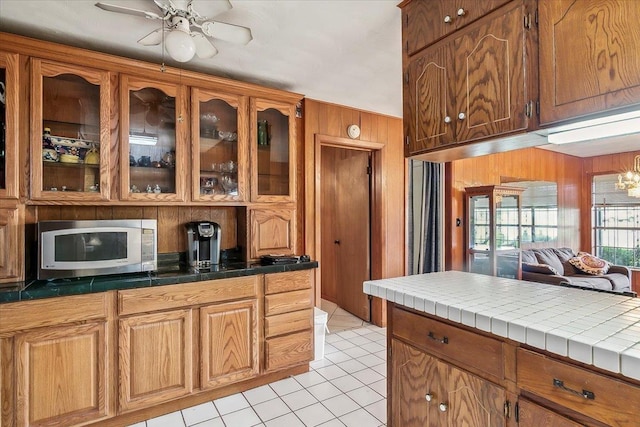 kitchen with wood walls, tile counters, light tile patterned floors, and ceiling fan with notable chandelier