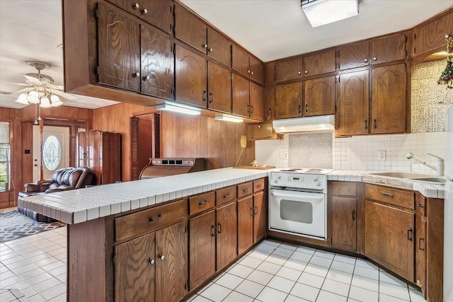 kitchen with kitchen peninsula, stove, tasteful backsplash, light tile patterned floors, and tile counters