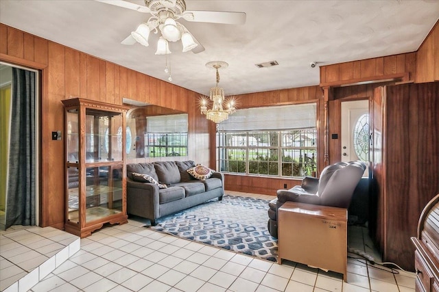 tiled living room with ceiling fan with notable chandelier, a healthy amount of sunlight, and wooden walls