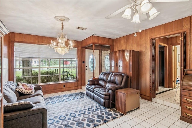 living room featuring wooden walls, light tile patterned floors, and ceiling fan with notable chandelier