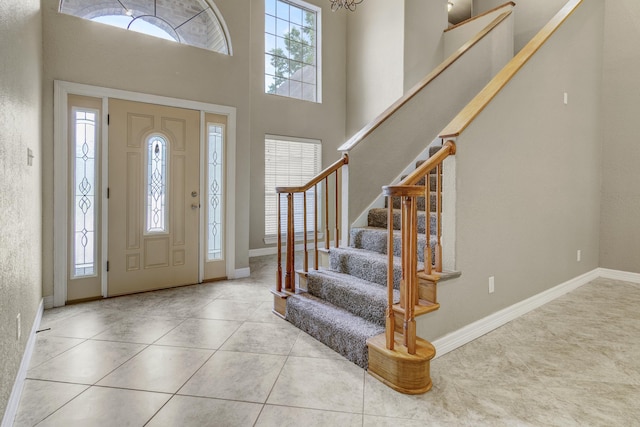 foyer entrance with light tile patterned floors, a towering ceiling, an inviting chandelier, and a wealth of natural light