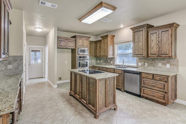 kitchen with sink, stainless steel appliances, light stone counters, decorative backsplash, and a kitchen island