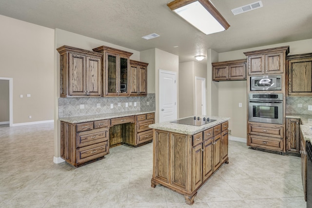 kitchen with a center island, light stone counters, backsplash, light tile patterned flooring, and black appliances