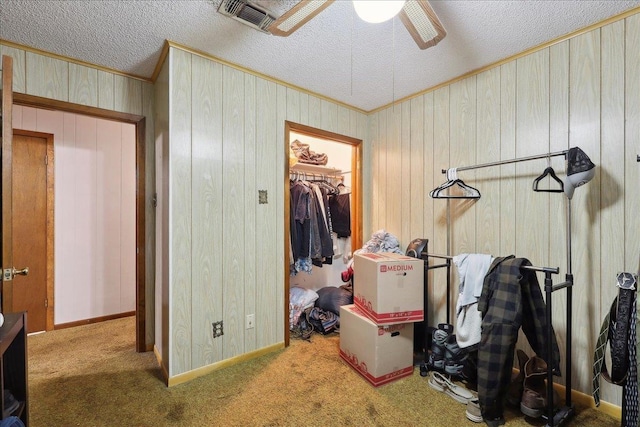 carpeted bedroom with a ceiling fan, a closet, a textured ceiling, a walk in closet, and crown molding