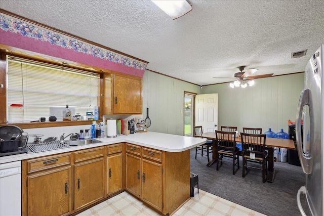 kitchen featuring a sink, freestanding refrigerator, brown cabinetry, light floors, and dishwasher