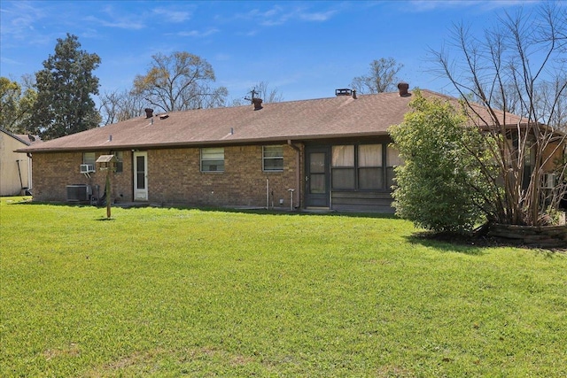 rear view of property with a lawn, central AC unit, brick siding, and roof with shingles