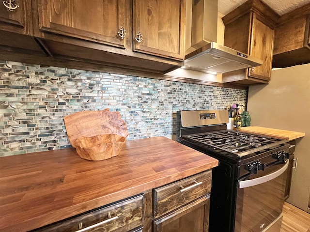 kitchen featuring wood counters, gas stove, tasteful backsplash, and wall chimney exhaust hood