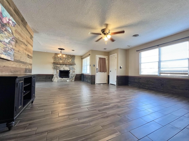 unfurnished living room with a stone fireplace, wood walls, and ceiling fan with notable chandelier