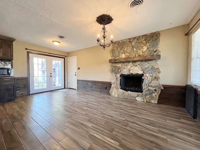 unfurnished living room featuring french doors, a textured ceiling, an inviting chandelier, and a stone fireplace