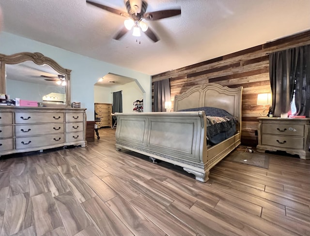 bedroom with ceiling fan, wood-type flooring, a textured ceiling, and wooden walls