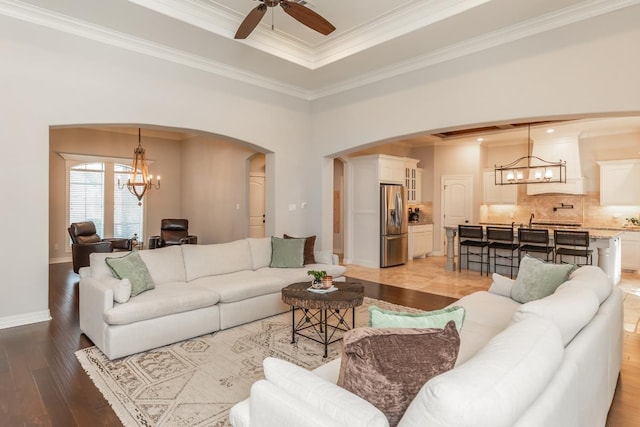 living room with wood-type flooring, a tray ceiling, ceiling fan with notable chandelier, and ornamental molding