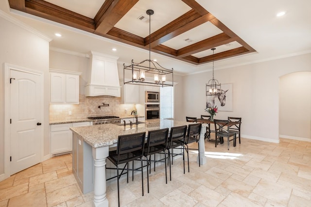 kitchen featuring white cabinets, premium range hood, stainless steel appliances, and a center island with sink