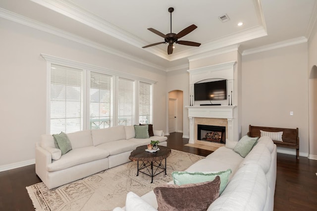 living room with hardwood / wood-style flooring, ceiling fan, a raised ceiling, a large fireplace, and crown molding