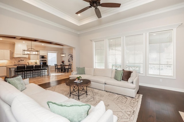 living room featuring ceiling fan with notable chandelier, a wealth of natural light, wood-type flooring, ornamental molding, and a tray ceiling