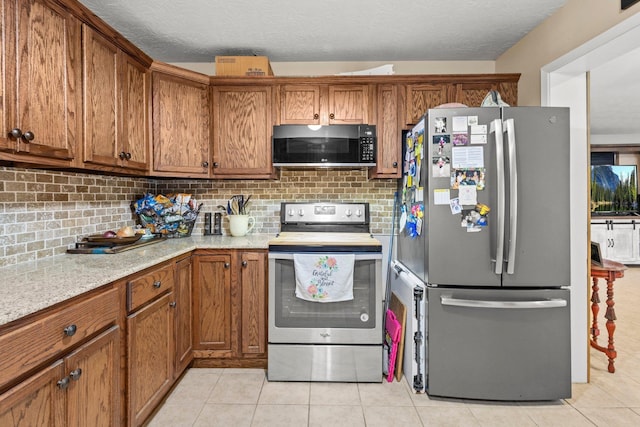 103 Read St, Silsbee, TX 77656 - kitchen with appliances with stainless steel finishes, brown cabinets, light tile patterned floors, and a textured ceiling