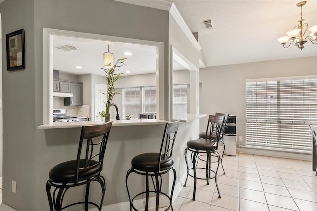 kitchen featuring gray cabinetry, stainless steel range, an inviting chandelier, tasteful backsplash, and a breakfast bar