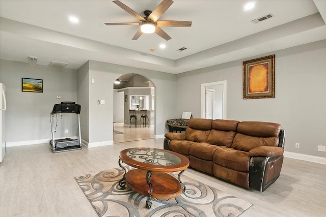 living room featuring light wood-type flooring, a raised ceiling, and ceiling fan