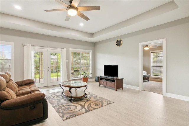 living room featuring a raised ceiling, a wealth of natural light, french doors, and ceiling fan