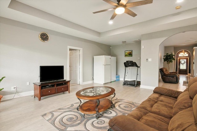 living room featuring a raised ceiling, ceiling fan, and light hardwood / wood-style flooring