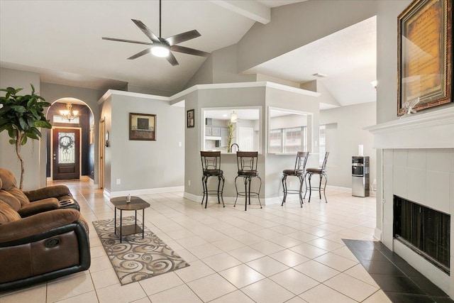 tiled living room featuring a tiled fireplace, lofted ceiling with beams, and ceiling fan with notable chandelier