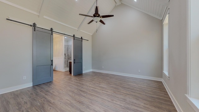 unfurnished bedroom with hardwood / wood-style flooring, high vaulted ceiling, connected bathroom, a barn door, and beamed ceiling